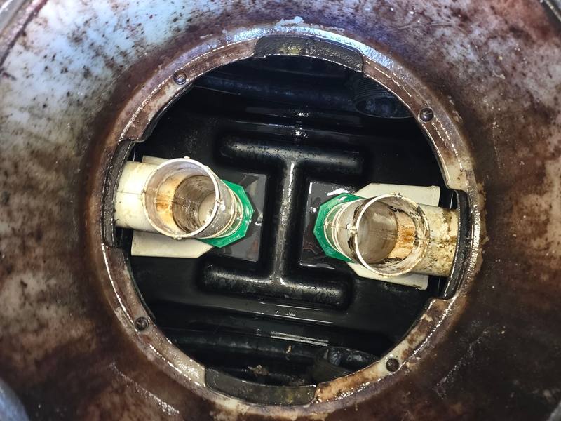 Looking down into an open grease interceptor, with a grease-stained rim, the black internal baffle and the inlet and outlet fittings