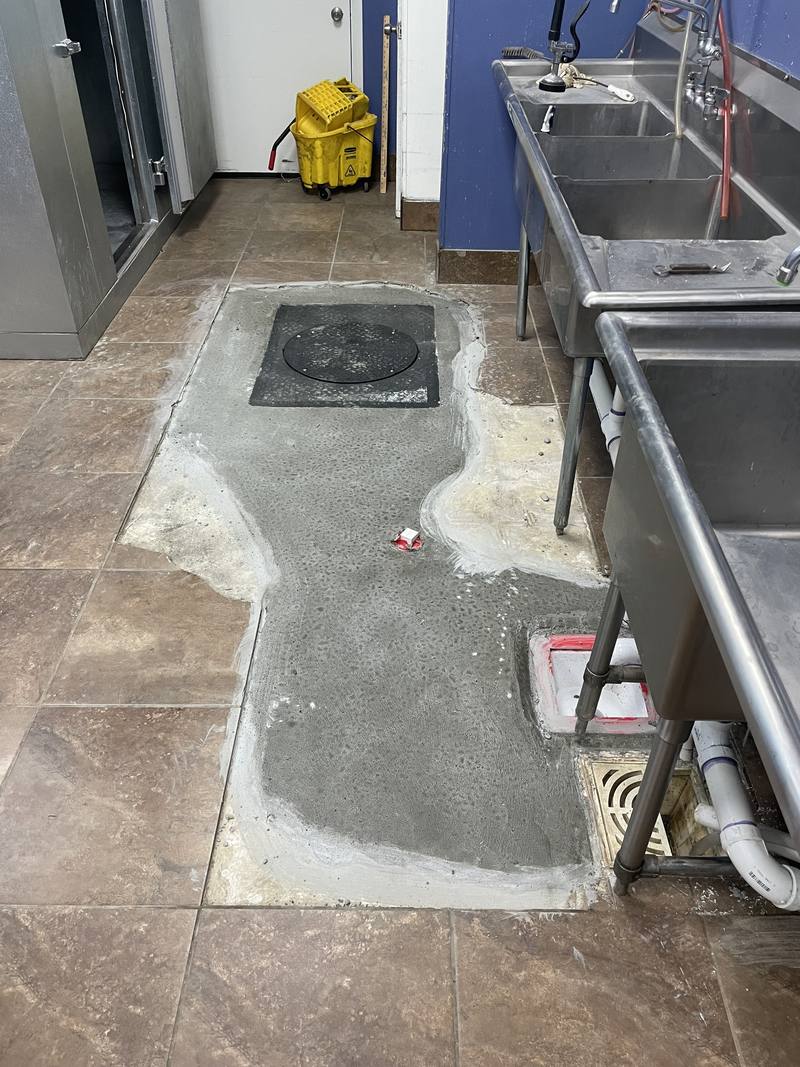 Finished kitchen floor with a fresh concrete patch and the interceptor lid set flush with the floor